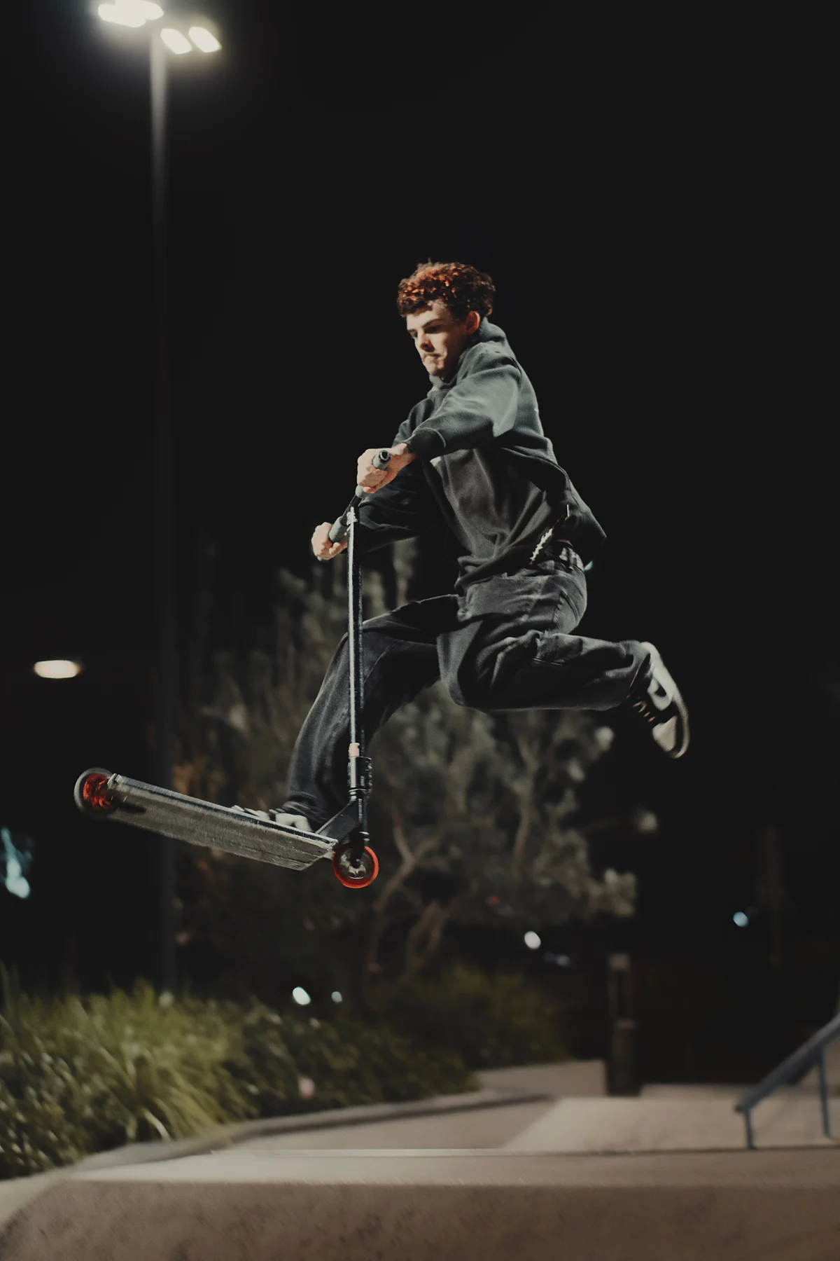 Scooter rider airborne at a skate park at night